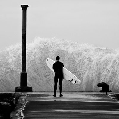 Fotografía en b/n ola y chico con tabla de surf